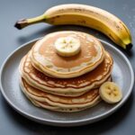 Pfannkuchen, nur leicht gebacken, auf einem Teller, daneben liegt eine Banane