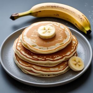 Pfannkuchen, nur leicht gebacken, auf einem Teller, daneben liegt eine Banane