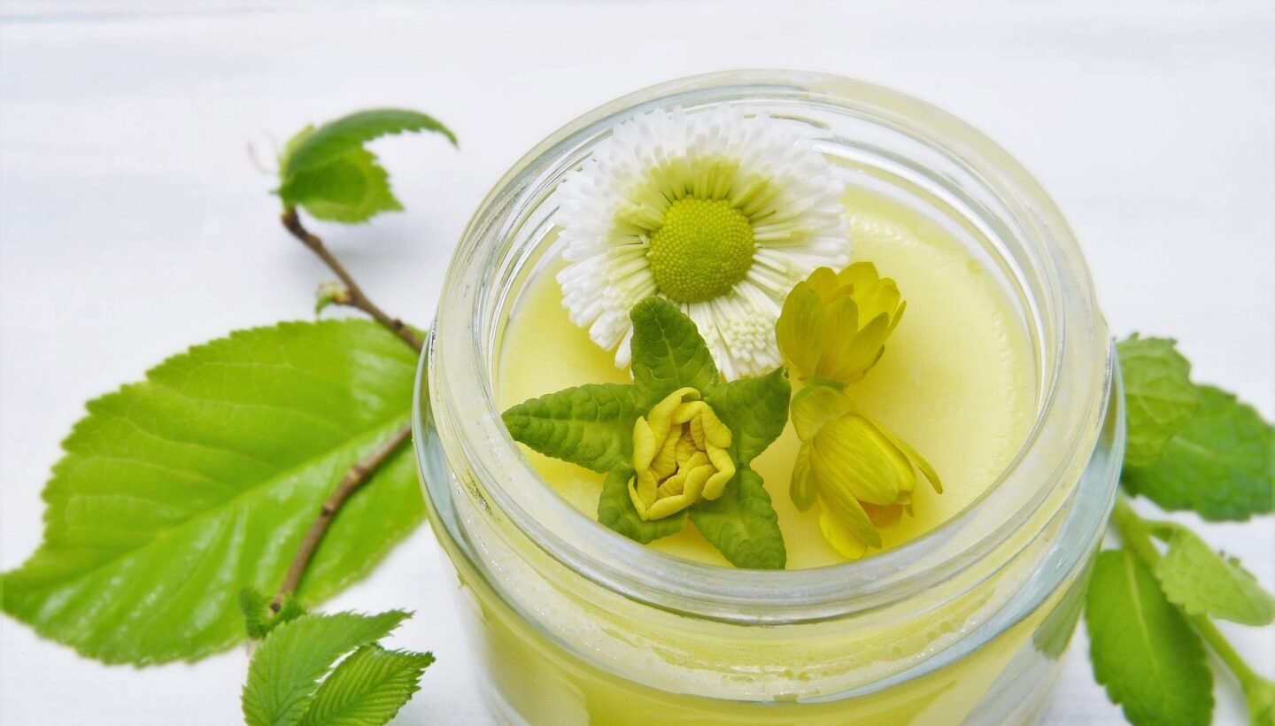 Ein Glastiegel mit Creme und Blüten, zur nachhaltigen Hautpflege